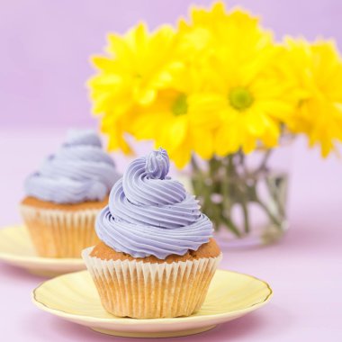 Cupcakes mor krem ve menekşe pastel zemin üzerine sarı Kasımpatı buket ile dekore edilmiştir. Metin alanı. Tebrik için ideal anneler gün ve Sevgililer kartı. En az natürmort kavramı.