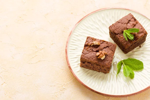 Brownie sweet chocolate dessert with walnuts and meant leaves on craft plate with copy space on pastel beige background - beautiful banner with delicious brown cocoa baked pastry.