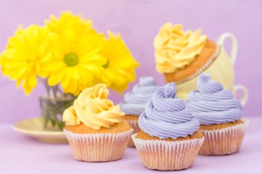 Sarı ve mor krem ve Kasımpatı Menekşe pastel arka planda tebrik kartı copyscape ile süslenmiş cupcakes.