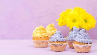 Sarı ve mor krem ve Kasımpatı Menekşe pastel arka planda tebrik kartı copyscape ile süslenmiş cupcakes.