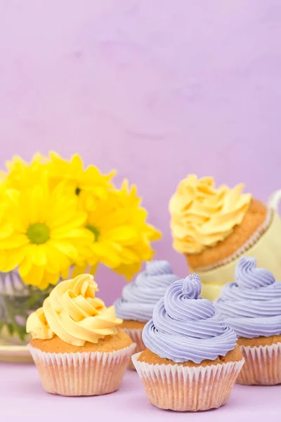 Cupcakes decorados com creme amarelo e violeta e crisântemos em fundo pastel violeta para cartão de saudação com copyscape . — Fotografia de Stock