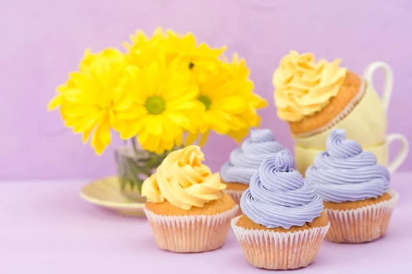 Cupcakes decorados con crema amarilla y violeta y crisantemos sobre fondo pastel violeta para tarjeta de felicitación con copyscape . — Foto de Stock
