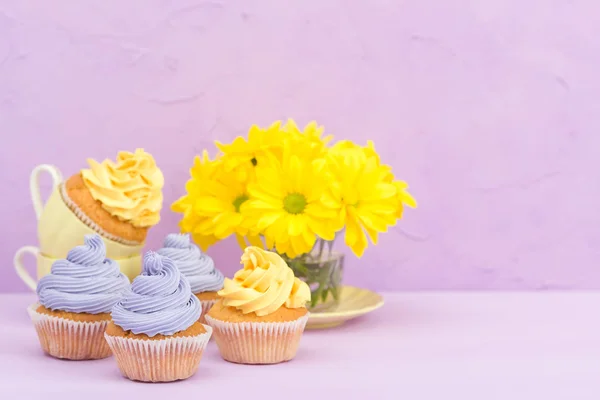 Cupcakes decorados com creme amarelo e violeta e crisântemos em fundo pastel violeta para cartão de saudação com copyscape . — Fotografia de Stock