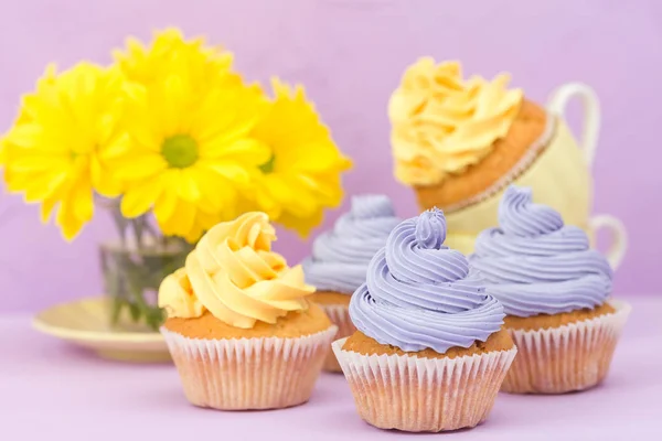 Cupcakes decorated with yellow and violet cream and chrysanthemums on violet pastel background for greeting card with copyscape. — Stock Photo, Image
