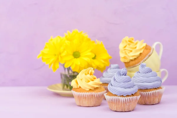 Cupcakes decorados com creme amarelo e violeta e crisântemos em fundo pastel violeta para cartão de saudação com copyscape . — Fotografia de Stock