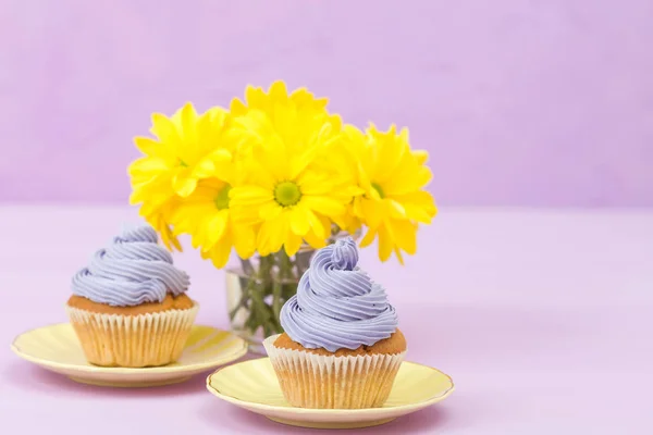 Cupcakes decorados con crema violeta y ramo de crisantemos amarillos sobre fondo pastel violeta con área de texto para saludo banner . — Foto de Stock