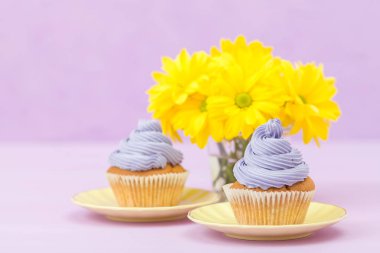 Cupcakes mor krem ve menekşe pastel zemin üzerine sarı Kasımpatı buket ile dekore edilmiştir. Metin alanı. Tebrik için ideal anneler gün ve Sevgililer kartı. En az natürmort kavramı.