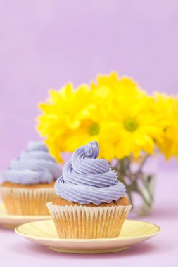 Cupcakes mor krem ve menekşe pastel zemin üzerine sarı Kasımpatı buket ile dekore edilmiştir. Metin alanı. Tebrik için ideal anneler gün ve Sevgililer kartı. En az natürmort kavramı.