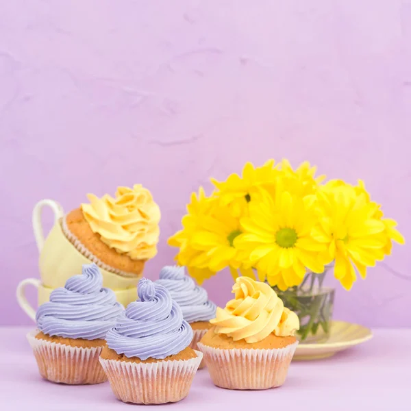 カップケーキは 甘い黄色と紫のクリームと紫色のパステル調の背景に菊の花で飾られました Copyspace エリア 挨拶に使える母の日やバレンタインのカード ミニマリズムのコンセプト — ストック写真