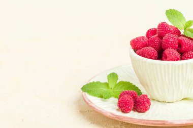 Olgun ahududu ile yeşil nane yaprakları Kupası ve fincan tabağı pastel sarı arka plan üzerinde - yaz mevsimlik ham meyveleri için sağlıklı organik beslenme kavramı makro fotoğraf kadar yakın.