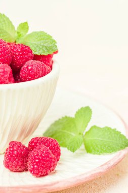 Olgun ahududu ile yeşil nane yaprakları Kupası ve fincan tabağı pastel sarı arka plan üzerinde - yaz mevsimlik ham meyveleri için sağlıklı organik beslenme kavramı makro fotoğraf kadar yakın.