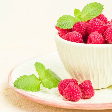 Olgun ahududu ile yeşil nane yaprakları Kupası ve fincan tabağı pastel sarı arka plan üzerinde - yaz mevsimlik ham meyveleri için sağlıklı organik beslenme kavramı makro fotoğraf kadar yakın.