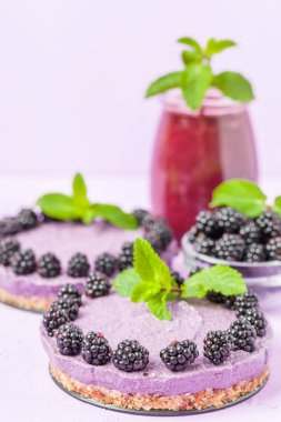 Ham blackberry tatlı taze olgun orman meyveleri ile dekore edilmiş ve yeşil nane yaprakları ve güler yüzlü pastel mor zemin - sağlıklı beslenme ve diyet kavramı için tatlı organik gıda üzerine karışık.