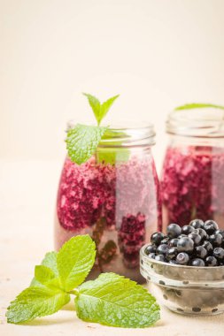 Taze yeşil nane yaprakları ve ham Olgun meyveleri yaz karışımlı vitamini kopya alanı ile kokteyl şeffaf kavanoz sarı pastel arka planda - Blueberry smoothie süslenmiş.