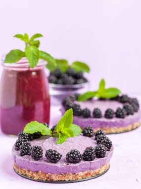 Ham blackberry tatlı taze olgun orman meyveleri ile dekore edilmiş ve yeşil nane yaprakları ve güler yüzlü pastel mor zemin - sağlıklı beslenme ve diyet kavramı için tatlı organik gıda üzerine karışık.
