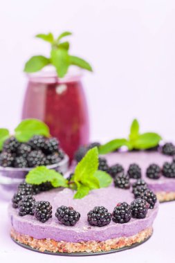 Ham blackberry tatlı taze olgun orman meyveleri ile dekore edilmiş ve yeşil nane yaprakları ve güler yüzlü pastel mor zemin - sağlıklı beslenme ve diyet kavramı için tatlı organik gıda üzerine karışık.