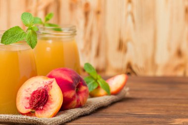 Taze olgunlaşmış meyve ve yeşil nane yaprakları ahşap arka plan - ham şekerli tatlı veya kahvaltı içki sağlıklı organik beslenme kavramı üzerinde cam kavanozlara şeftali yüzlü.