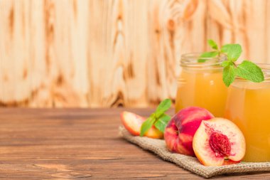 Taze olgunlaşmış meyve ve yeşil nane yaprakları ahşap arka plan - ham şekerli tatlı veya kahvaltı içki sağlıklı organik beslenme kavramı üzerinde cam kavanozlara şeftali yüzlü.