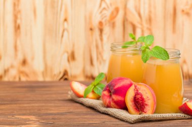 Taze olgunlaşmış meyve ve yeşil nane yaprakları ahşap arka plan - ham şekerli tatlı veya kahvaltı içki sağlıklı organik beslenme kavramı üzerinde cam kavanozlara şeftali yüzlü.