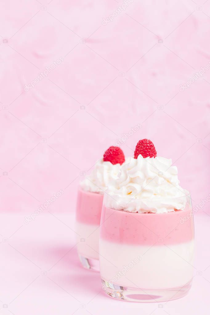 Raspberry panna cotta decorated with cream and ripe berry on pastel pink background - close up photography of sweet dairy dessert with summer fruits in beautiful glasses.