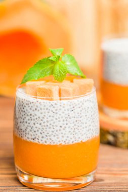 Chia puding güzel gözlük yeşil nane yaprakları ve kahverengi ahşap arka plan - ham vejetaryen tatlı sağlıklı organik tatlı taze olgun sebze ile kabak püresi ile.