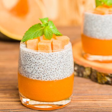 Chia puding güzel gözlük yeşil nane yaprakları ve kahverengi ahşap arka plan - ham vejetaryen tatlı sağlıklı organik tatlı taze olgun sebze ile kabak püresi ile.