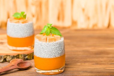 Chia puding güzel gözlük yeşil nane yaprakları ve kahverengi ahşap arka plan - ham vejetaryen tatlı sağlıklı organik tatlı taze olgun sebze ile kabak püresi ile.