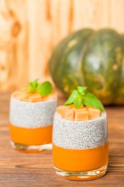 Chia puding güzel gözlük yeşil nane yaprakları ve kahverengi ahşap arka plan - ham vejetaryen tatlı sağlıklı organik tatlı taze olgun sebze ile kabak püresi ile.