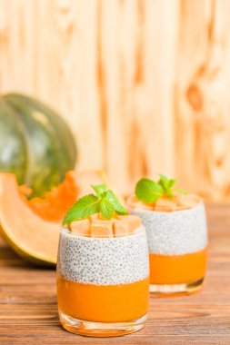 Chia puding güzel gözlük yeşil nane yaprakları ve kahverengi ahşap arka plan - ham vejetaryen tatlı sağlıklı organik tatlı taze olgun sebze ile kabak püresi ile.