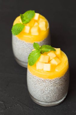 Chia tohum puding mango ile güzel gözlük yeşil nane yaprakları ile püre ve siyah arka plan - ham vejetaryen şekerli organik tatlı karanlık ruh tarzı üzerine taze olgun tropikal meyve kesme.