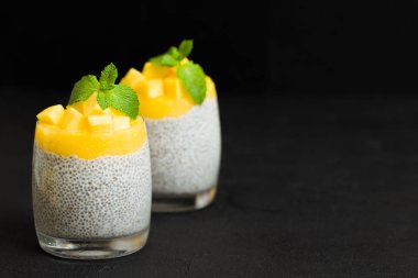 Chia tohum puding mango ile güzel gözlük yeşil nane yaprakları ile püre ve siyah arka plan - ham vejetaryen şekerli organik tatlı karanlık ruh tarzı üzerine taze olgun tropikal meyve kesme.