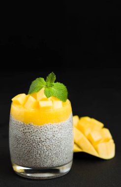 Chia tohum puding mango ile güzel gözlük yeşil nane yaprakları ile püre ve siyah arka plan - ham vejetaryen şekerli organik tatlı karanlık ruh tarzı üzerine taze olgun tropikal meyve kesme.