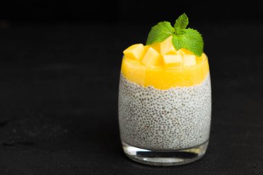 Chia tohum puding mango ile güzel gözlük yeşil nane yaprakları ile püre ve siyah arka plan - ham vejetaryen şekerli organik tatlı karanlık ruh tarzı üzerine taze olgun tropikal meyve kesme.