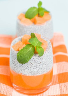 Chia tohum puding kabak ile güzel gözlük yeşil nane yaprakları ile püre ve pastel mavi arka plan - ham vejetaryen şekerli organik tatlı taze olgun turuncu sebze kesme.