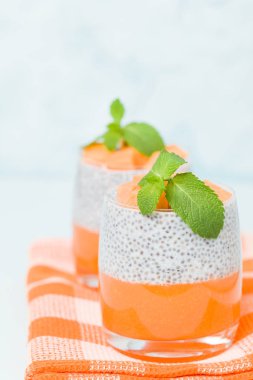 Chia tohum puding kabak ile güzel gözlük yeşil nane yaprakları ile püre ve pastel mavi arka plan - ham vejetaryen şekerli organik tatlı taze olgun turuncu sebze kesme.