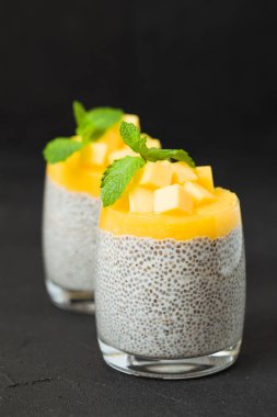 Chia tohum puding mango ile güzel gözlük yeşil nane yaprakları ile püre ve siyah arka plan - ham vejetaryen şekerli organik tatlı karanlık ruh tarzı üzerine taze olgun tropikal meyve kesme.