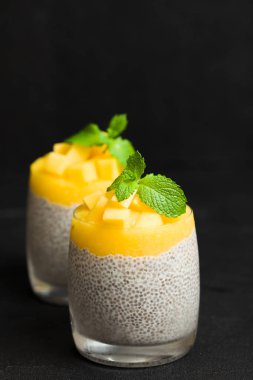 Chia tohum puding mango ile güzel gözlük yeşil nane yaprakları ile püre ve siyah arka plan - ham vejetaryen şekerli organik tatlı karanlık ruh tarzı üzerine taze olgun tropikal meyve kesme.