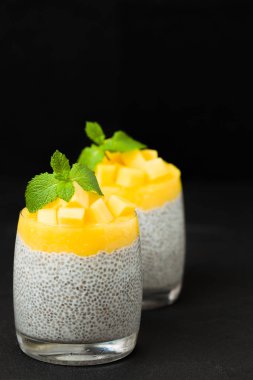 Chia tohum puding mango ile güzel gözlük yeşil nane yaprakları ile püre ve siyah arka plan - ham vejetaryen şekerli organik tatlı karanlık ruh tarzı üzerine taze olgun tropikal meyve kesme.
