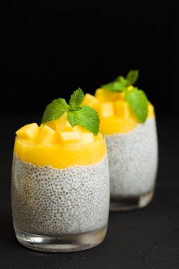 Chia tohum puding mango ile güzel gözlük yeşil nane yaprakları ile püre ve siyah arka plan - ham vejetaryen şekerli organik tatlı karanlık ruh tarzı üzerine taze olgun tropikal meyve kesme.
