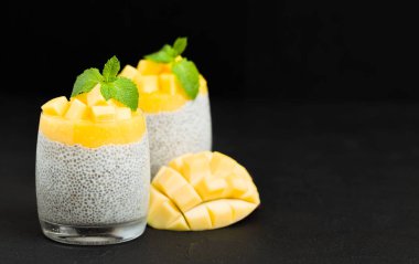 Chia tohum puding mango ile güzel gözlük yeşil nane yaprakları ile püre ve siyah arka plan - ham vejetaryen şekerli organik tatlı karanlık ruh tarzı üzerine taze olgun tropikal meyve kesme.