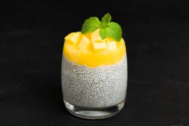 Chia tohum puding mango ile güzel gözlük yeşil nane yaprakları ile püre ve siyah arka plan - ham vejetaryen şekerli organik tatlı karanlık ruh tarzı üzerine taze olgun tropikal meyve kesme.