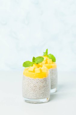 Chia tohum puding mango ile güzel gözlük yeşil nane yaprakları ile püre ve pastel mavi arka plan - ham vejetaryen şekerli organik tatlı taze olgun tropikal meyve kesme.