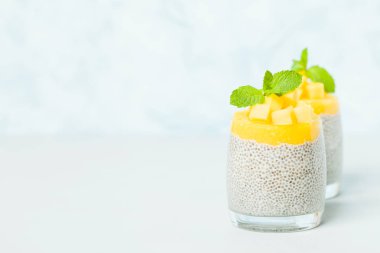 Chia tohum puding mango ile güzel gözlük yeşil nane yaprakları ile püre ve pastel mavi arka plan - ham vejetaryen şekerli organik tatlı taze olgun tropikal meyve kesme.