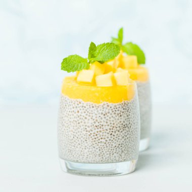 Chia tohum puding mango ile güzel gözlük yeşil nane yaprakları ile püre ve pastel mavi arka plan - ham vejetaryen şekerli organik tatlı taze olgun tropikal meyve kesme.