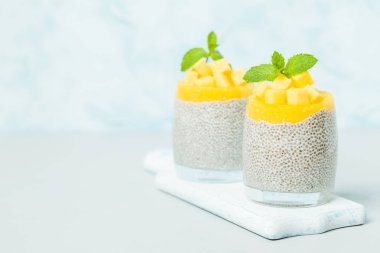 Chia tohum puding mango ile güzel gözlük yeşil nane yaprakları ile püre ve pastel mavi arka plan - ham vejetaryen şekerli organik tatlı taze olgun tropikal meyve kesme.