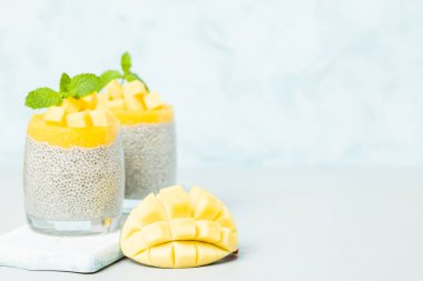 Chia tohum puding mango ile güzel gözlük yeşil nane yaprakları ile püre ve pastel mavi arka plan - ham vejetaryen şekerli organik tatlı taze olgun tropikal meyve kesme.