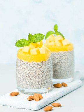 Chia tohum puding mango ile badem süt güzel gözlük yeşil nane yaprakları ile püre ve pastel mavi arka plan - ham vejetaryen şekerli organik tatlı taze olgun tropikal meyve kesme.