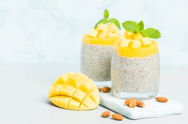 Chia tohum puding mango ile badem süt güzel gözlük yeşil nane yaprakları ile püre ve pastel mavi arka plan - ham vejetaryen şekerli organik tatlı taze olgun tropikal meyve kesme.