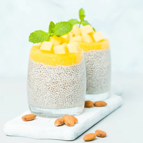 Chia tohum puding mango ile badem süt güzel gözlük yeşil nane yaprakları ile püre ve pastel mavi arka plan - ham vejetaryen şekerli organik tatlı taze olgun tropikal meyve kesme.