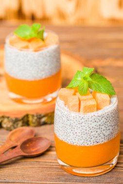 Chia puding güzel gözlük yeşil nane yaprakları ve kahverengi ahşap arka plan - ham vejetaryen tatlı sağlıklı organik tatlı taze olgun sebze ile kabak püresi ile.